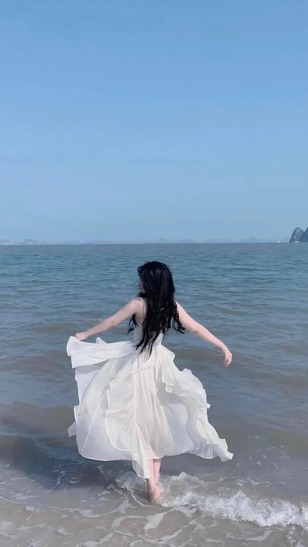 anh-gai-di-bien-che-mat-13 Cô gái bước nhanh trên bờ cát, tà váy tung nhẹ, dáng lưng thon, vibe mùa hè.