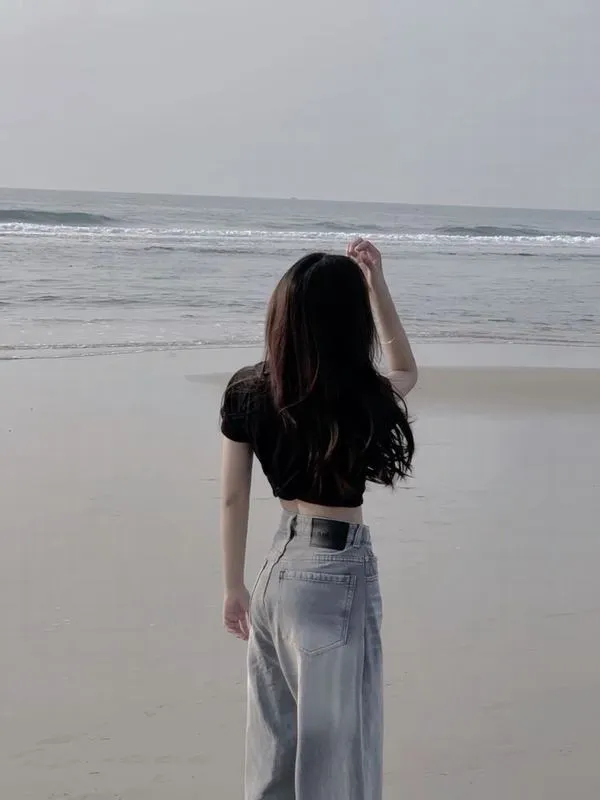 anh-gai-di-bien-che-mat-2 Cô gái quay lưng trên bãi biển, tóc dài bay nhẹ, dáng đứng mảnh, mood yên ả.