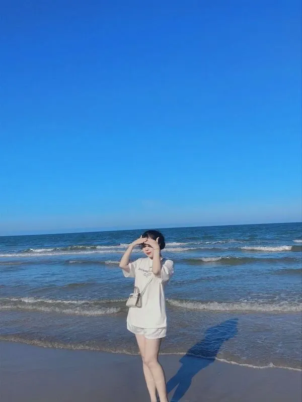 anh-gai-di-bien-che-mat-6 Nàng mặc đồ sáng màu, đứng dưới ánh nắng, một tay che mặt, đường nét dịu dàng.